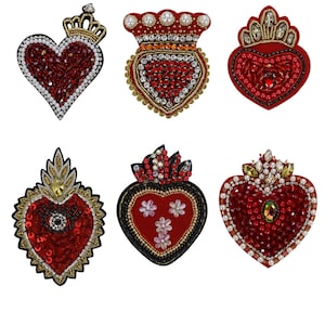 Puede incluir: Seis parches bordados en forma de corazón rojo con adornos dorados y plateados. Cada parche presenta un diseño diferente, incluyendo coronas, llamas y flores.