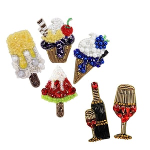 May include: A selection of beaded brooches depicting desserts and wine. The brooches feature an ice cream cone, a popsicle, a watermelon popsicle, a wine bottle with a glass, and a wine glass. The brooches are decorated with beads in various colours.
