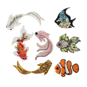 Puede incluir: Una colección de broches de peces con cuentas en varios colores y diseños. Los broches incluyen un pez plateado, un pez negro con gemas azules y transparentes, un pez rojo y blanco, un pez rosa, un pez verde y azul, un pez dorado y un pez payaso naranja y blanco.