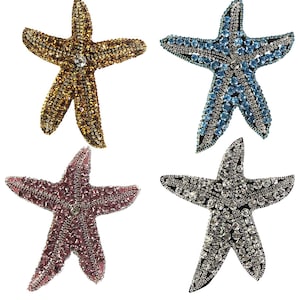 May include: Four rhinestone starfish embellishments in different colors: gold, blue, pink, and silver. Each starfish is approximately 2 inches in diameter.