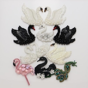 Puede incluir: Una colección de parches bordados con diversas aves, incluyendo cisnes blancos y negros, un flamenco rosa y un pavo real verde. Cada parche está adornado con cuentas, lentejuelas y cristales, mostrando texturas intrincadas y diseños detallados.