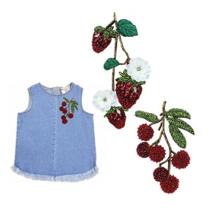 Può includere: Un vestito senza maniche in denim blu chiaro con orlo sfilacciato. L'abito presenta un design a ciliegia ricamato sul davanti. Sono presenti anche decorazioni decorative di rami di fragole e ciliegie con perline e accenti floreali bianchi.