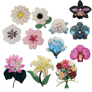 May include: A selection of beaded flower brooches. The brooches feature diverse floral designs, including daisies, orchids, and lilies, with detailed beadwork in colours such as pink, white, and blue. These brooches are suitable for adorning garments or accessories.