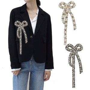 以下が含まれることがあります： 長い尾のついたラインストーンのボウブローチ2つ。1つのブローチはクリアなラインストーンでシルバー、もう1つは白いパールでシルバーです。