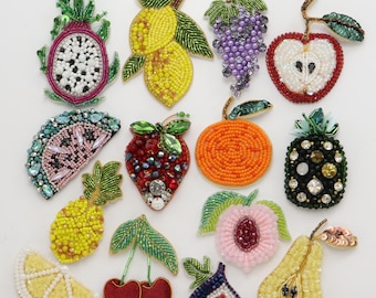 May include: A collection of fourteen fruit-shaped patches crafted with colorful glass beads, sequins, and crystals. The assortment includes a dragon fruit, lemons, grapes, an apple, watermelon, strawberry, orange, pineapple, cherry, peach, fig, and pear.