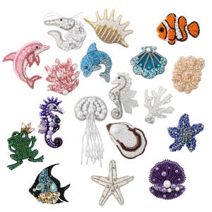 May include: A selection of beaded ocean-themed embellishments, including a pink dolphin, blue seahorse, and orange clownfish. Other designs include a frog, jellyfish, and coral. The collection features a variety of sea creatures, each intricately detailed with beads.