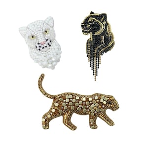 Peut inclure: Trois broches animales perlées : une tête de chat blanche, une panthère noire avec des accents dorés et un léopard doré et marron. Les broches sont finement détaillées et probablement destinées aux vêtements ou accessoires.
