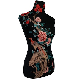 Könnte beinhalten: Eine schwarze Stoffapplikation mit einem detaillierten Stickmuster eines Vogels, der auf einem Zweig mit rosa, roten und grünen Blumen sitzt.