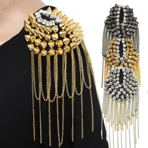 Könnte beinhalten: Goldene, silberne und schwarze Schulterkette mit Spikes und Strasssteinen. Die Kette hat ein langes, herabhängendes Design mit mehreren Strängen.