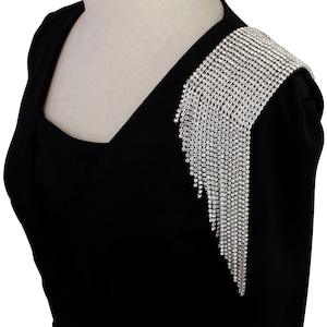 Può includere: Un blazer nero con un lungo dettaglio di frangia di strass argentati sulla spalla.