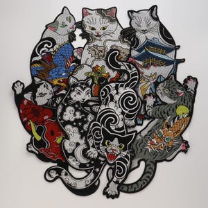 May include: A large embroidered patch featuring a cluster of cats in various poses, integrated with traditional motifs including a blue dragon, a red mask, a pagoda, and swirling cloud patterns in black, white, grey, and vibrant colours.
