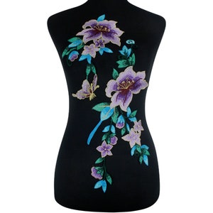 Könnte beinhalten: Violette und blaue gestickte Blumenapplikation mit Schmetterlingsmotiv. Diese Applikation ist perfekt, um Kleidung, Taschen oder Heimtextilien einen Hauch von Eleganz zu verleihen.