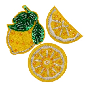 Puede incluir: Tres parches de limón bordados. Un limón entero con hojas verdes, una rodaja de limón y una rodaja de limón redonda. Los parches son amarillos con costuras blancas y algunas lentejuelas.
