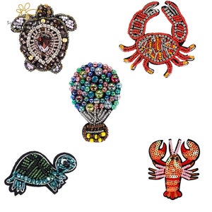 May include: Five colourful beaded iron-on patches. The patches include a hot air balloon, a turtle, a crab, and a lobster. The patches are perfect for adding a touch of whimsy to clothing, bags, or other fabric items.