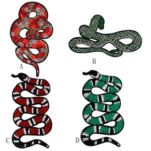 May include: Four embroidered snake patches in different colors and designs. The patches are made of beads and fabric. The snakes are in red, green, and black.