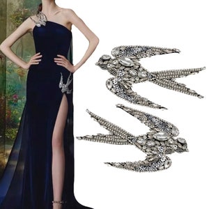 May include: Two silver and crystal embellished swallow bird appliques. The birds are in flight with their wings spread out. The appliques are perfect for adding a touch of sparkle to any garment or project.