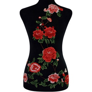May include: Red embroidered floral applique with green leaves on a black background. The applique features a vine of red roses with white centers.