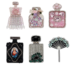 Puede incluir: Seis broches diferentes de frasco de perfume con cuentas y joyas. Las broches son de varios colores y estilos, incluyendo rosa, negro, blanco y verde. Algunas de las broches presentan una imagen religiosa, mientras que otras presentan flores o un abanico.