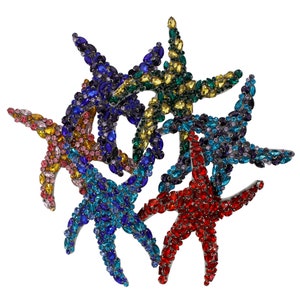Puede incluir: Un grupo de seis estrellas de mar de colores, cada una cubierta de brillantes piedras de cristal. Las estrellas de mar están dispuestas en un patrón circular, con las puntas de cada estrella superpuestas. Los colores de las piedras de cristal incluyen rojo, azul, verde, amarillo y morado.