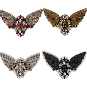 May include: Four embroidered patches featuring a pair of wings with a jeweled center. The patches are in four different color combinations: red, gold, black, and silver.