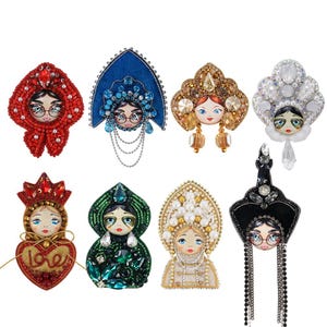 May include: A collection of eight handmade brooches featuring stylized doll faces with glasses. Each brooch showcases intricate beadwork in various colors, including red, blue, gold, and green, with pearl and crystal accents. The brooches are designed with elaborate headpieces.