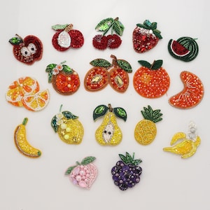 Op de afbeelding: Een collectie van zeventien fruitvormige patches, vervaardigd met kleurrijke glaskralen, pailletten en kristallen. De set bevat afbeeldingen van appels, kersen, aardbeien, watermeloen, sinaasappels, citroenen, peren, ananassen, bananen, perziken en bramen.