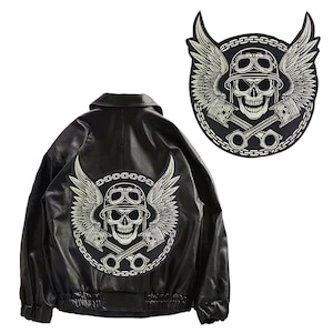 Puede incluir: Chaqueta de cuero negra con un parche bordado en plata de un cráneo y alas en la espalda. El parche presenta un cráneo con casco y gafas, con llaves inglesas y pistones cruzados.