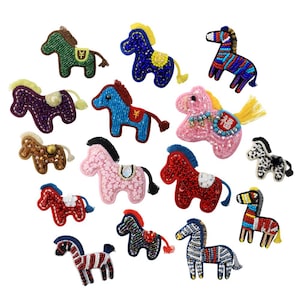 Könnte beinhalten: Eine Sammlung von Pferdefiguren aus Perlen in verschiedenen Farben, darunter Grün, Blau, Rosa und Rot. Jedes Pferd hat ein einzigartiges Design mit Details wie Sätteln und Mähnen. Die Figuren sind auf weißem Hintergrund angeordnet.