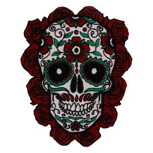 Könnte beinhalten: Weißer Zucker Schädel mit grünen und roten floralen Details, umgeben von roten Rosen.