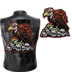 Può includere: Un paio di toppe da stirare con un'aquila di cartone animato che indossa occhiali e porta uno zaino, appollaiata su una pila di teschi. L'aquila è marrone, gialla e arancione. I teschi sono bianchi e grigi.