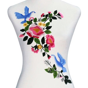May include: Embroidered applique featuring two blue birds perched on a leafy branch with pink and white flowers. The design is perfect for adding a touch of nature to clothing, bags, or home decor.
