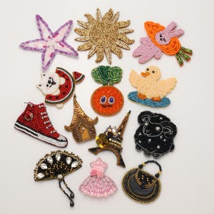 May include: A collection of assorted beaded patches featuring various shapes including a purple starfish, gold sun, orange carrot, red sneaker, black sheep, Eiffel Tower, pink dress, black fan, and a duck, all crafted with intricate glass seed beads.