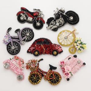 May include: A collection of eight beaded patches featuring various vehicles and bicycles. The set includes two motorcycles, a red car, a yellow bicycle with flowers, a pink car with flowers, a black bicycle, and two pink floral-themed vehicles.