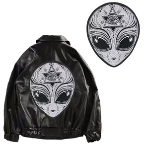 Pode incluir: Etiqueta de ferro bordada em preto e branco de um alienígena com um terceiro olho em um triângulo. O alienígena tem olhos grandes e um design detalhado.