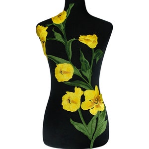 Puede incluir: Aplique de flores bordadas de color amarillo con hojas verdes. El aplique está sobre un fondo negro.