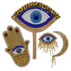 May include: Three embroidered patches featuring the evil eye symbol. The first patch is a large blue eye with gold beads and sequins. The second patch is a gold hand with a blue eye in the palm. The third patch is a crescent moon with a blue eye and gold beads.