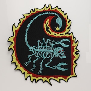 May include: An embroidered patch featuring a light blue skeletal scorpion with a skull head and red eyes. The scorpion is set against a black background, surrounded by a red border and a jagged yellow flame-like edge with a small yellow star.