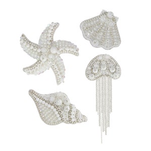 Könnte beinhalten: Vier weiße Perlen- und Strass-besetzte Broschen mit Meeresmotiven. Die Broschen sind ein Seestern, eine Muschel, eine Venusmuschel und eine Qualle.