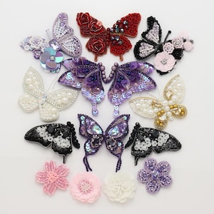 May include: A collection of decorative butterfly and flower patches featuring intricate beadwork, sequins, and crystals. The assortment includes various colors such as red, purple, black, white, and pink, showcasing detailed embroidery and embellishments.