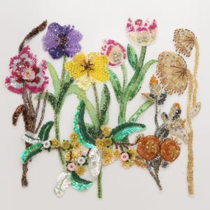 May include: A decorative applique featuring a collection of embroidered flowers crafted with colorful beads and sequins. The design includes purple, yellow, pink, and orange blossoms with green stems and leaves, accented by metallic gold and silver beadwork.