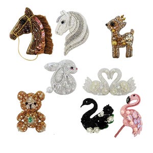May include: A collection of beaded animal brooches, including a horse, deer, rabbit, teddy bear, swans, a black swan, and a flamingo. The brooches feature various colors and textures, with intricate beadwork and embellishments.