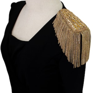 May include: Black blazer with a gold shoulder embellishment featuring a fringe design and a rectangular rhinestone detail.