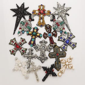Puede incluir: Una colección de parches decorativos con diversas formas de cruces y estrellas. Estos apliques están adornados con pedrería, cuentas y cristales de colores en tonos negro, plata, oro, rojo, azul, verde y blanco, dispuestos en patrones intrincados.