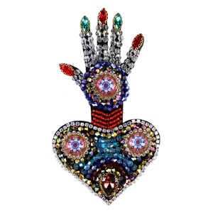 May include: A hand and heart shaped brooch with colorful crystal embellishments. The hand is raised with fingers spread and the heart is below it. The brooch is made of black fabric with red, blue, and green crystals.