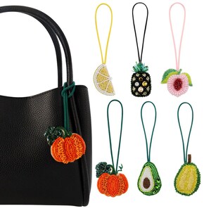 May include: A black leather handbag with a beaded pumpkin charm attached to the zipper pull. The image also shows five other beaded charms: a lemon, a pineapple, a peach, a pumpkin, and an avocado.