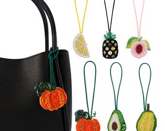 May include: A black leather handbag with a beaded pumpkin charm attached to the zipper pull. The image also shows five other beaded charms: a lemon, a pineapple, a peach, a pumpkin, and an avocado.