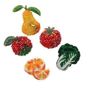 May include: A collection of beaded fruit and vegetable pins. The pins include a pear, apple, tomato, orange slices, and a leafy green vegetable. The pear is yellow and orange, the apple is red and green, and the tomato is red. The orange slices are orange and white.