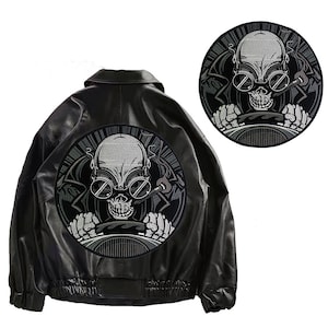 May include: A black leather jacket with a round, embroidered patch on the back. The patch features a skull wearing goggles and driving a car.