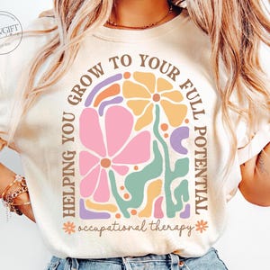 May include: A white t-shirt with a colorful graphic design that says "Helping you grow to your full potential *occupational therapy*" in a retro font.