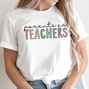 Puede incluir: Camiseta blanca con el texto "parents as TEACHERS" en colores arco&iacute;ris.